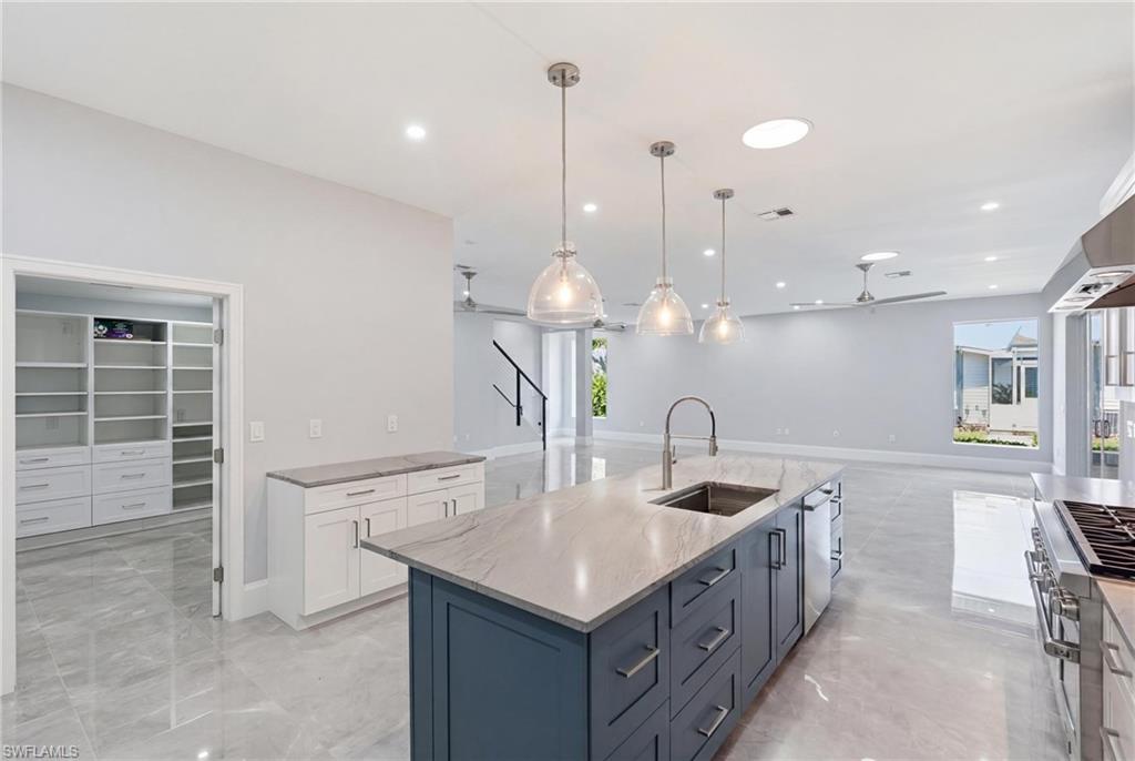 Open-concept kitchen featuring a large island with a stainless steel sink and blue cabinetry, pendant lighting, professional-grade range, and light gray tile flooring