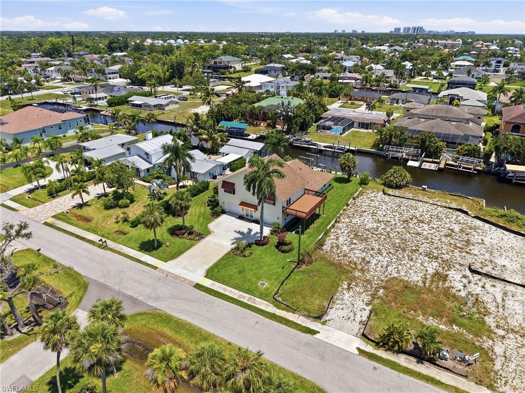 Waterfront property featuring a two-story residence with a balcony, manicured lawn, and mature palm trees