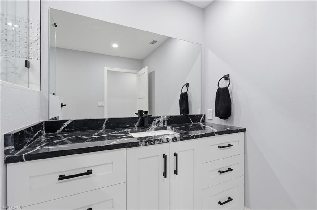 Contemporary bathroom vanity featuring a black patterned countertop, white cabinetry with black hardware, and a large wall-mounted mirror
