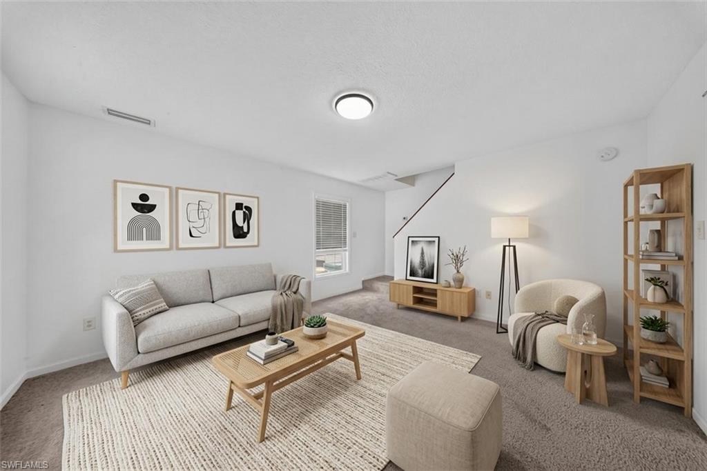 Carpeted living area featuring white walls, a visible window with blinds, and a staircase