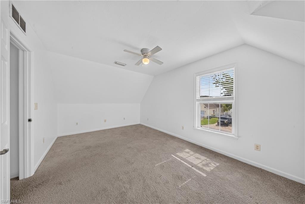 Attic room featuring neutral carpeting, a white ceiling fan, a single window with blinds, and white walls