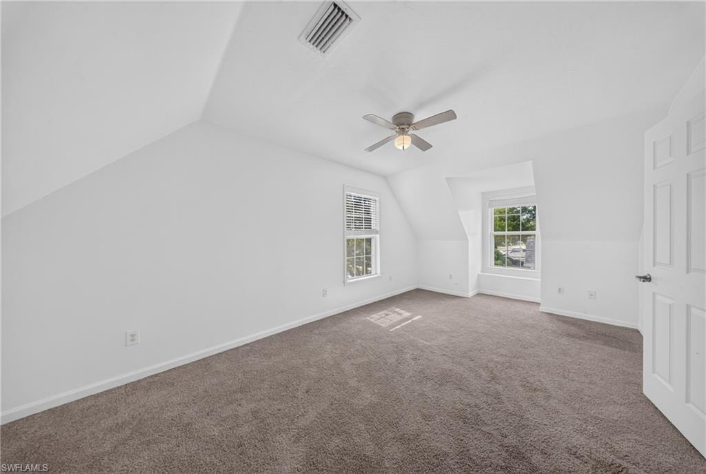 Spacious room featuring neutral carpeting, white painted walls, and a ceiling fan with integrated lighting