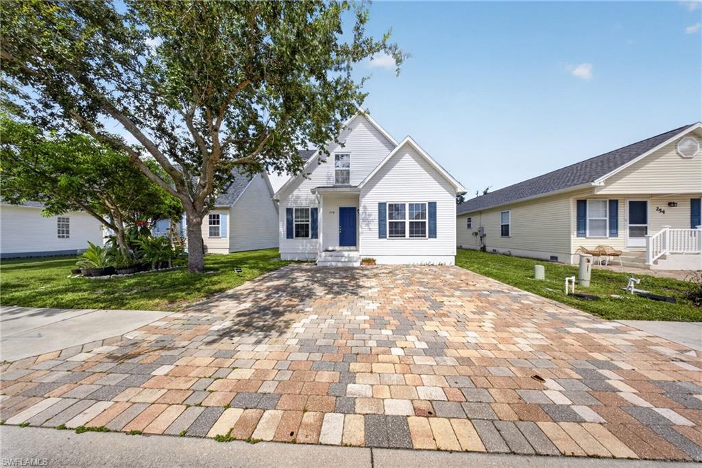 White exterior with blue shutters, a paver driveway, mature trees, and a front entry