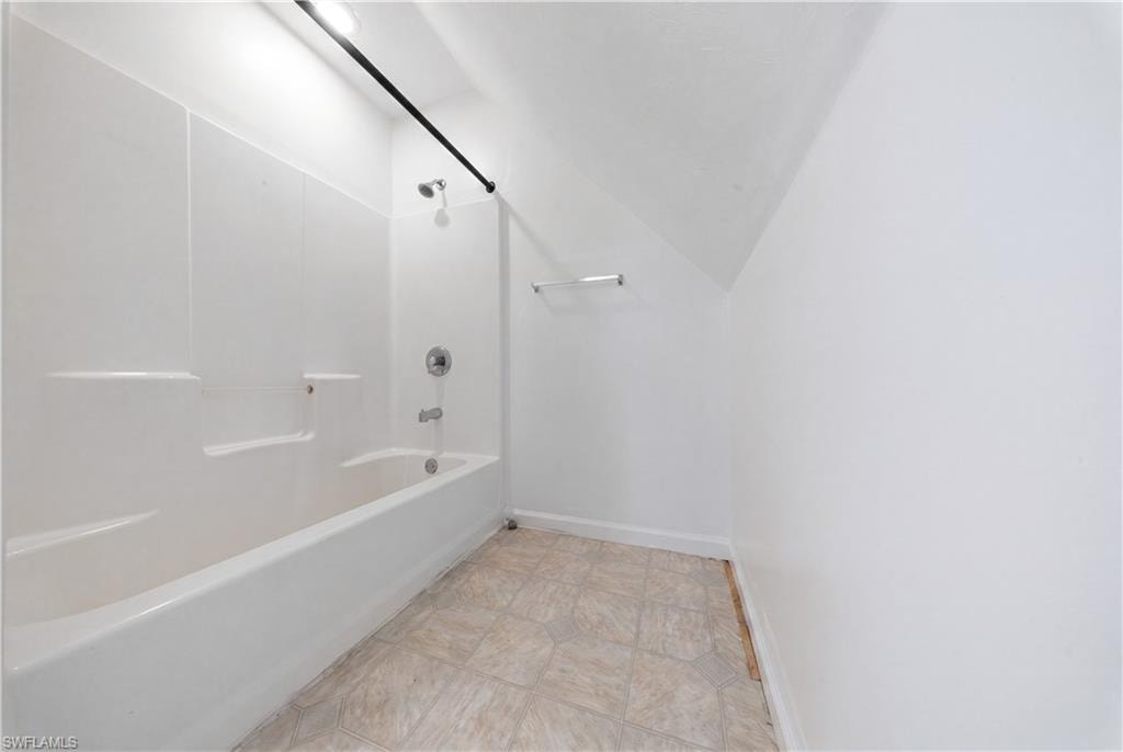 Bathtub with integrated shower surround, stainless steel shower fixtures, and a ceiling-mounted light fixture