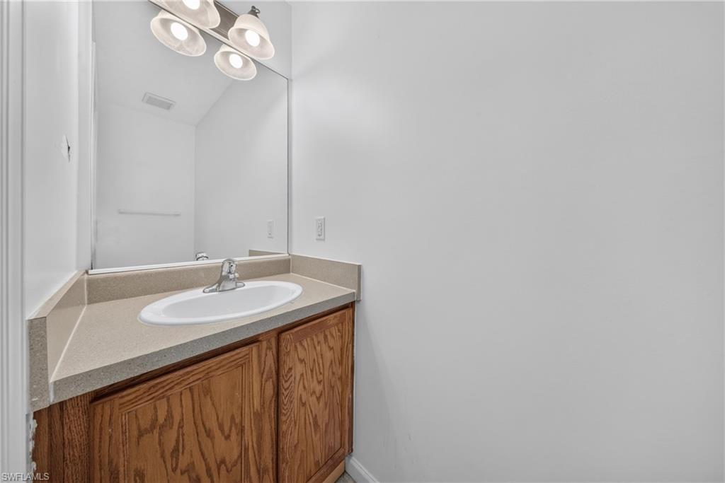 Vanity with wood-finish cabinetry, a neutral countertop, and an undermount sink