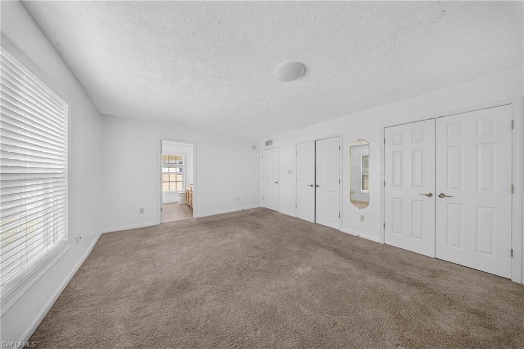 Carpeted room with multiple paneled doors, a window with horizontal blinds, and a flush-mount ceiling light fixture