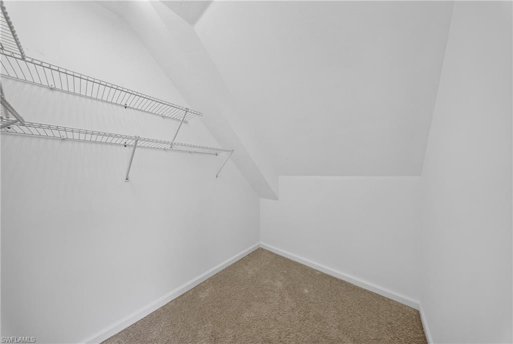 Storage area featuring white walls, sloped ceiling, light-colored carpet flooring, and two levels of wire shelving