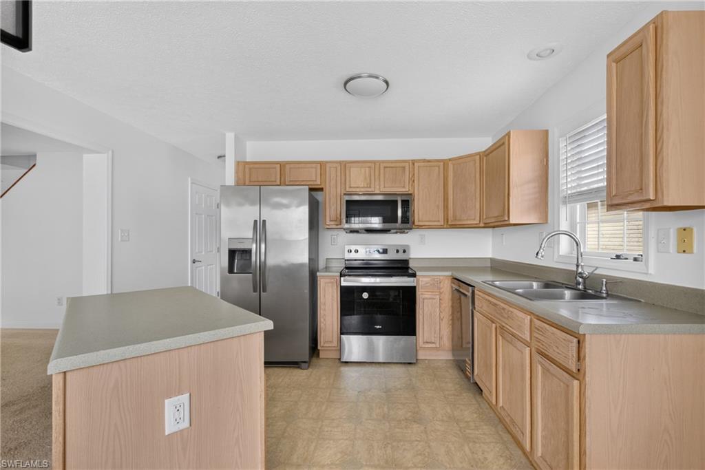 Kitchen featuring stainless steel appliances, light wood cabinetry, and a central island with a solid surface countertop