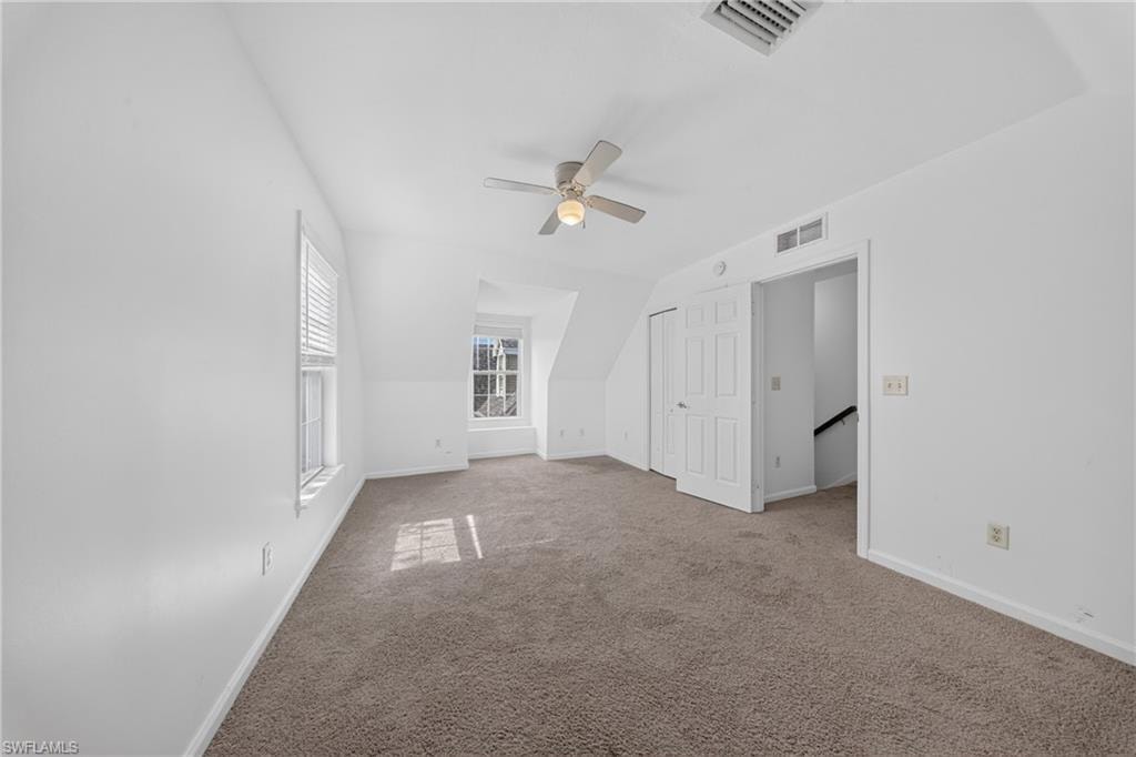 Carpeted room featuring white walls, multiple windows with blinds, a ceiling fan with integrated lighting, and a bi-fold closet door