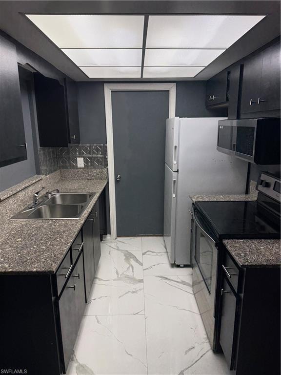 Galley kitchen with dark cabinetry, granite-finish countertops, stainless steel double basin sink, and white marbling-effect tile flooring