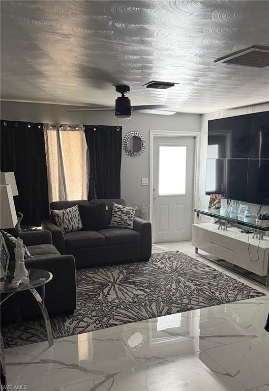 Living area featuring polished marble-look flooring, a ceiling fan with integrated lighting, a contrasting dark accent wall, and a white paneled door