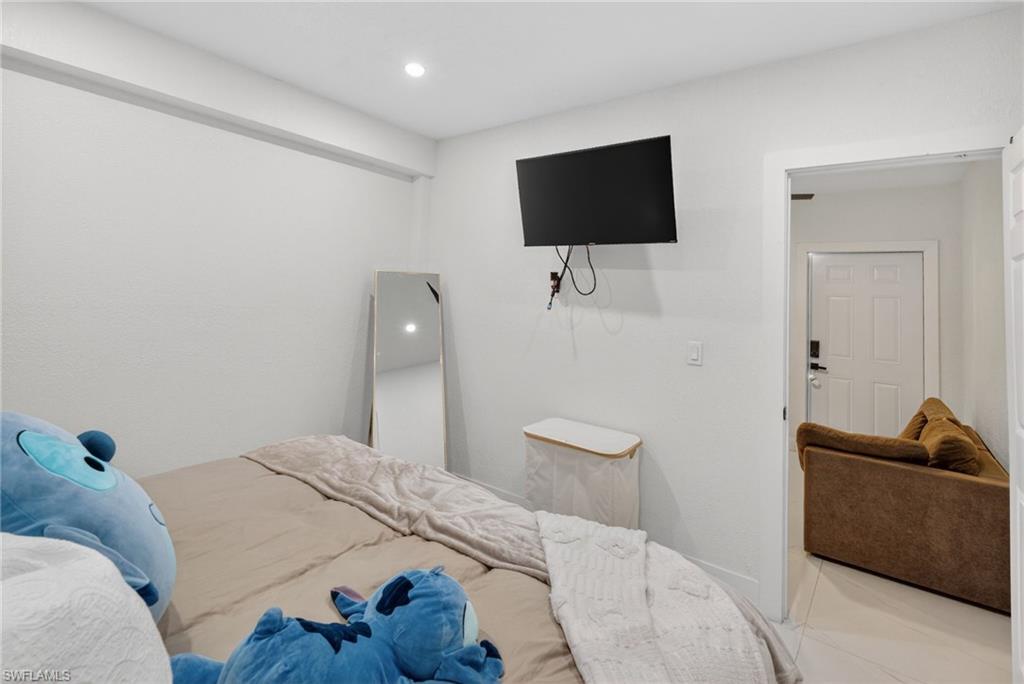 Recessed lighting illuminates a bright interior with white walls, a wall-mounted television, and a white paneled door