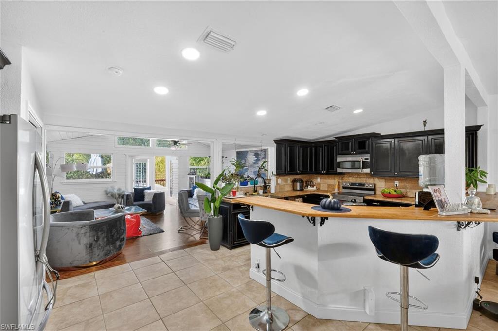 Open concept interior featuring tile flooring in the kitchen, wood-finish flooring in the living area, recessed lighting, black cabinetry, and a wood-finish countertop