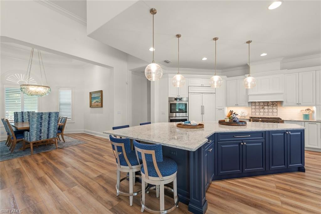 Gourmet kitchen featuring a large island with seating, white shaker cabinetry, stainless steel appliances, and wood-finish flooring
