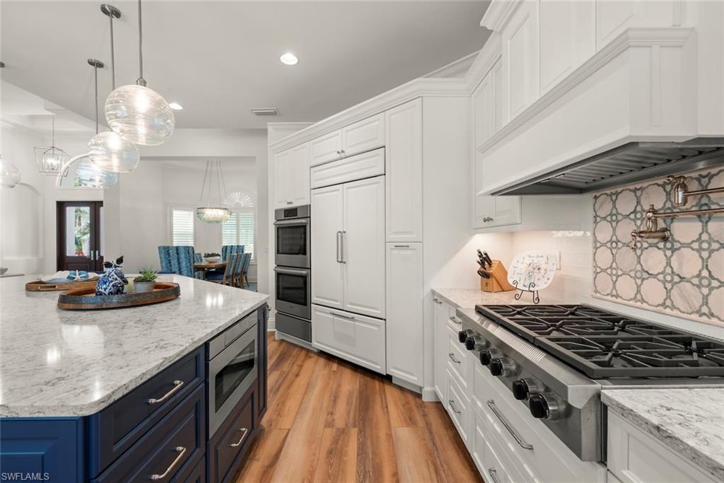 Gourmet kitchen featuring a gas range, a decorative tile backsplash, double wall ovens, a built-in refrigerator, and an island with stone countertops and pendant lighting