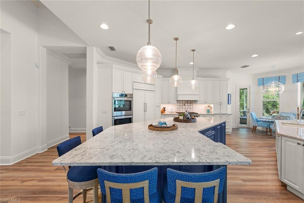 Spacious kitchen featuring a large island with a light-colored countertop, built-in double oven, paneled refrigerator, wood-finish flooring, and pendant lighting