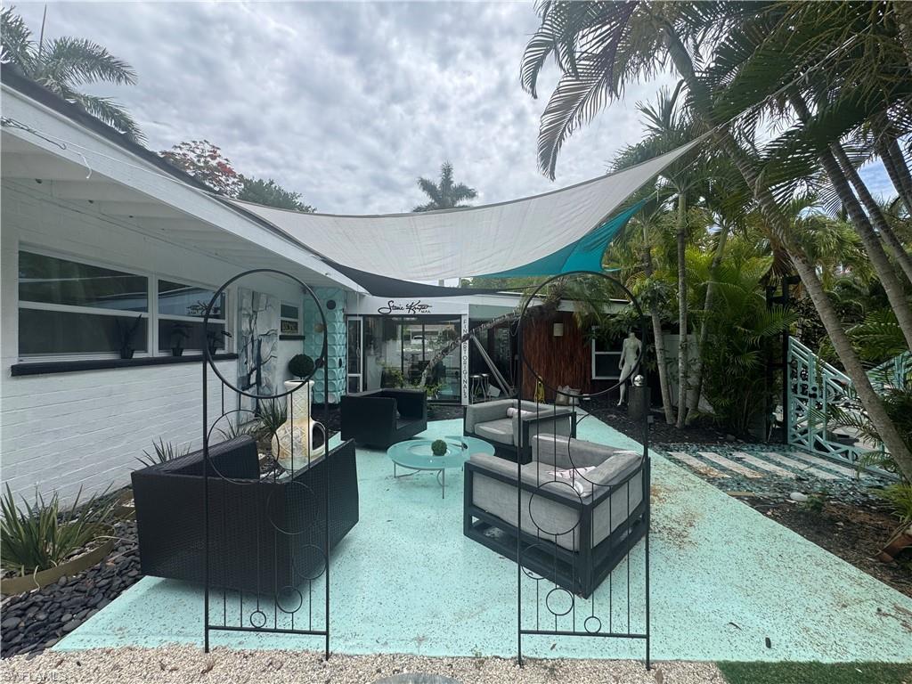 Outdoor living space featuring a shade sail, patterned concrete patio, and lush tropical landscaping