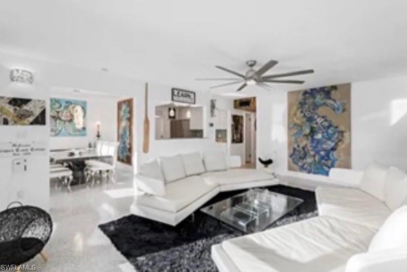 Bright living area featuring light-toned flooring, a modern ceiling fan, and a pass-through opening to an additional room