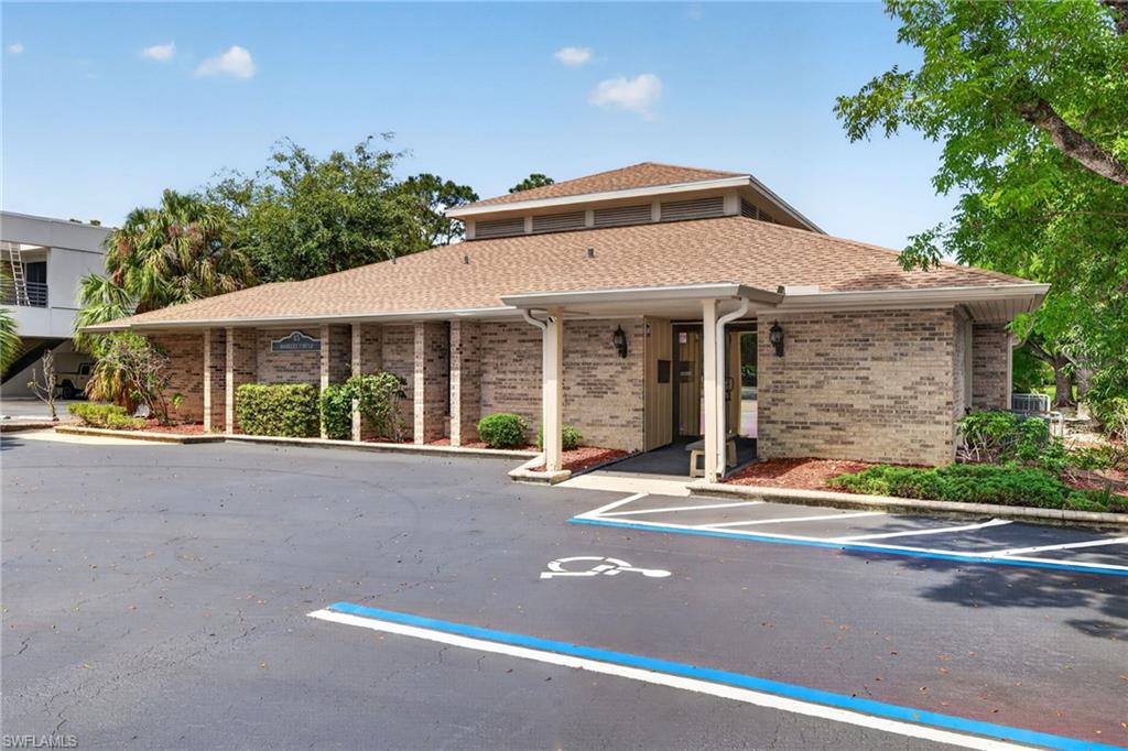 Brick exterior building featuring a brown shingle roof, covered entrance, wall sconces, and mature landscaping