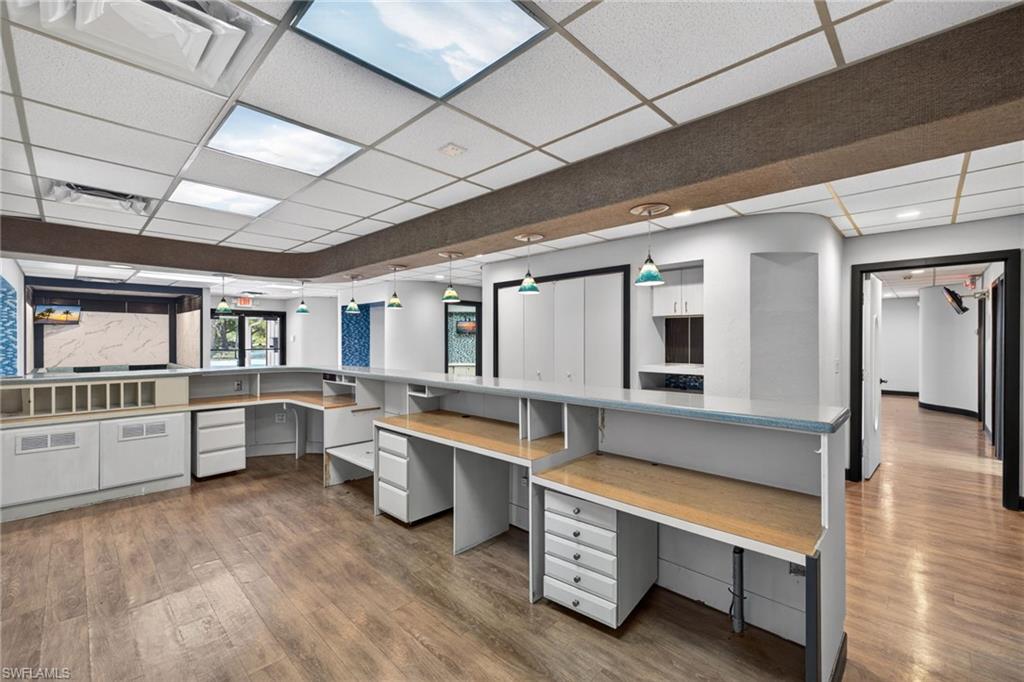 Reception area with built-in cabinetry, wood-finish flooring, drop ceiling with integrated lighting, and multiple workstations