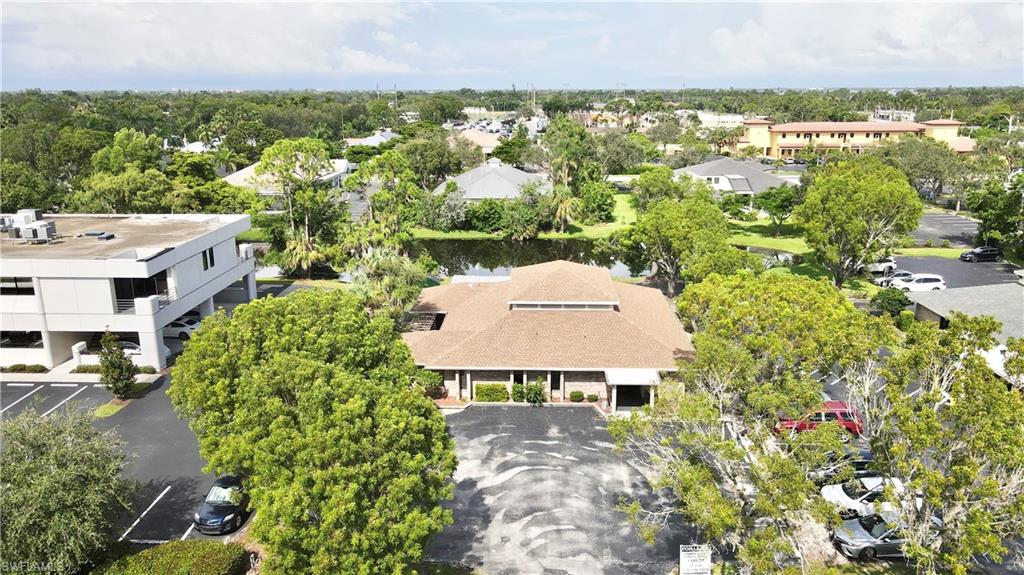 Single-story commercial building featuring a brown shingle roof, multiple entryways, and abundant mature landscaping