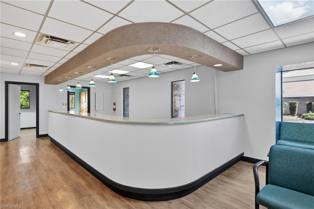 Reception area featuring a curved service counter with overhead pendant lighting, wood-finish flooring, and recessed ceiling lighting