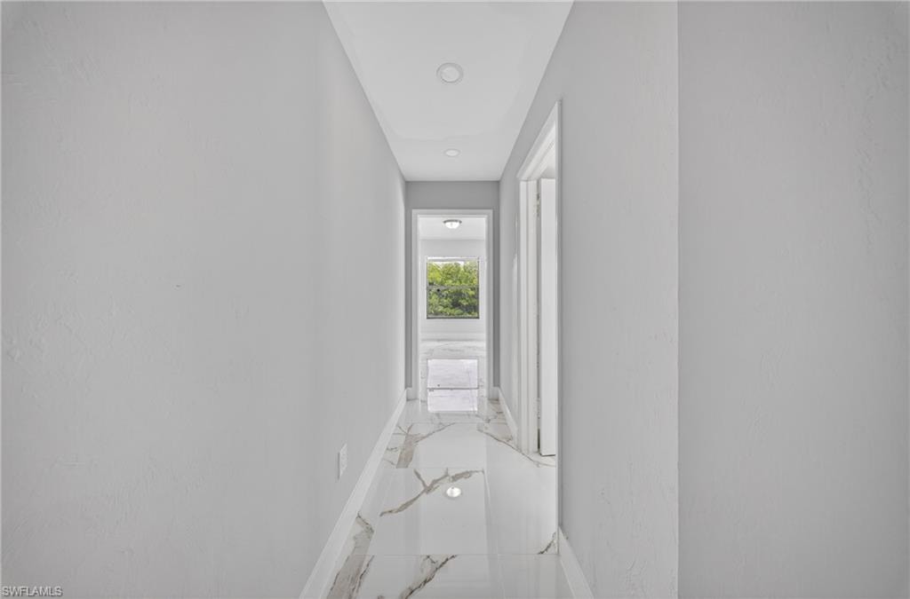 Hallway featuring marble-look tile flooring, light gray walls, recessed lighting, and white door frames