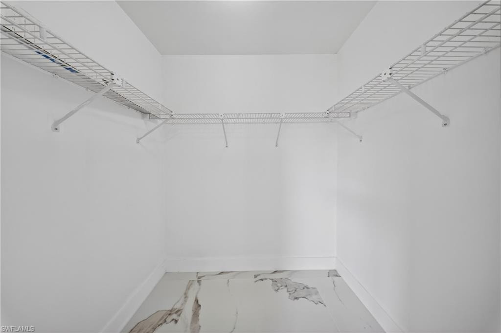 Walk-in closet featuring white wire shelving, white wall paint, white baseboards, and marble-look tile flooring