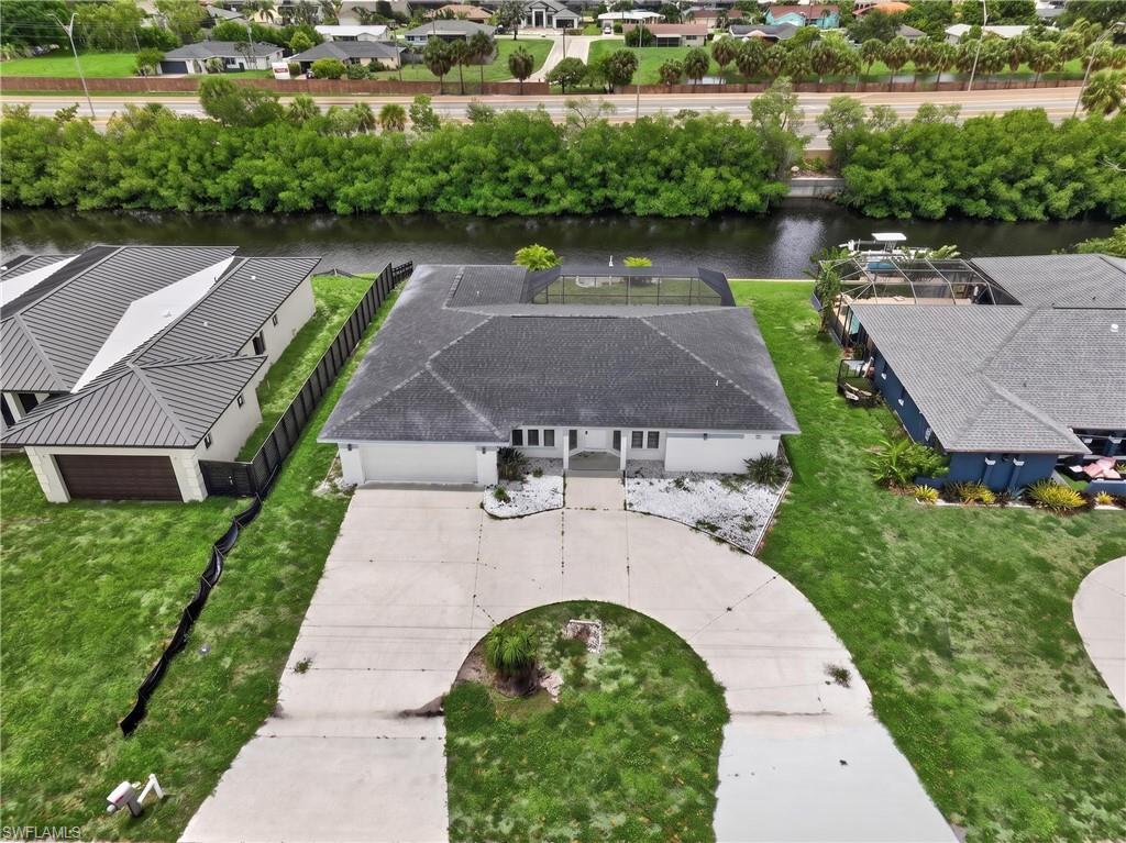 Canal-front property featuring a screened pool enclosure, curved driveway, and a two-car garage