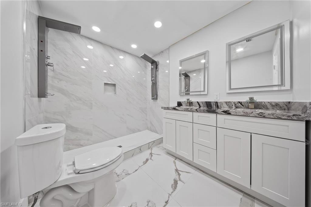 Contemporary bathroom featuring a spacious shower with multiple showerheads, a tiled bench, and a recessed niche