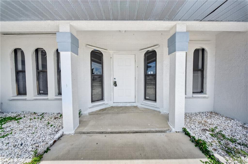 Exterior featuring an entry alcove, a white entry door, arched windows, and white decorative rock landscaping