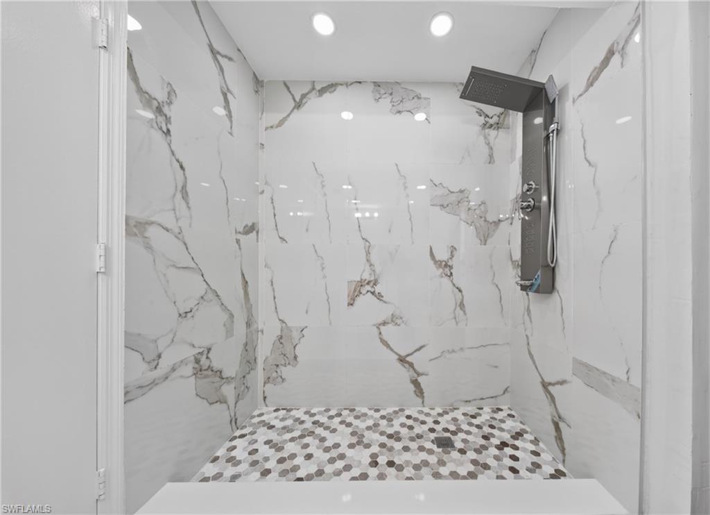 Shower featuring large format white and gray veined wall tiles, a multi-function shower panel with overhead rain shower, recessed lighting, and a mosaic tiled shower bench