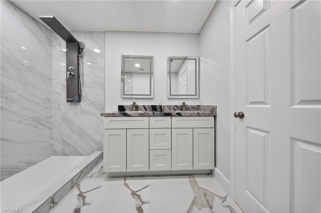 Modern bathroom featuring a spacious walk-in shower with a rainfall showerhead, dual vanity with white shaker-style cabinetry, dark speckled countertops, and framed mirrors