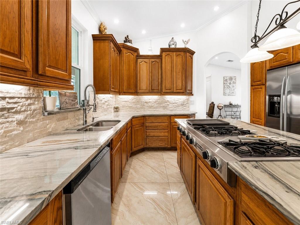 Kitchen featuring wood cabinetry, stone countertops, a tile backsplash, stainless steel appliances, and tile flooring
