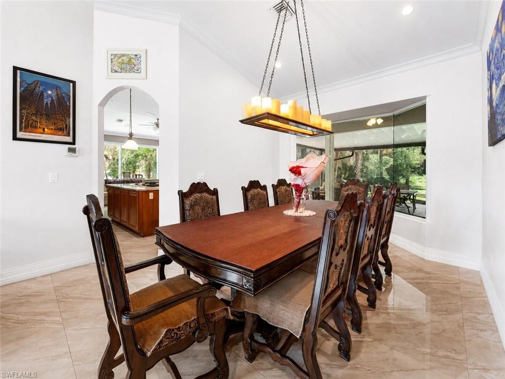 Spacious dining area featuring vaulted ceilings, a rectangular chandelier with faux candle lighting, and a large bay window overlooking outdoor landscaping
