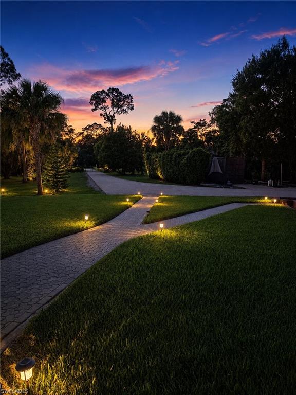 Expansive grounds featuring a paver pathway, lush lawn, and mature trees