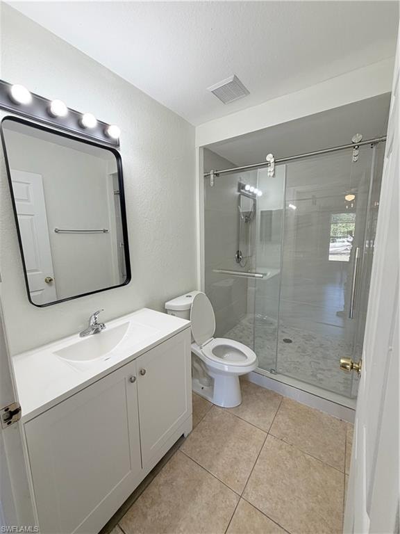 Full bathroom featuring a white vanity with integrated sink, a frameless shower enclosure with sliding glass doors, a single-handle chrome faucet, and tiled flooring