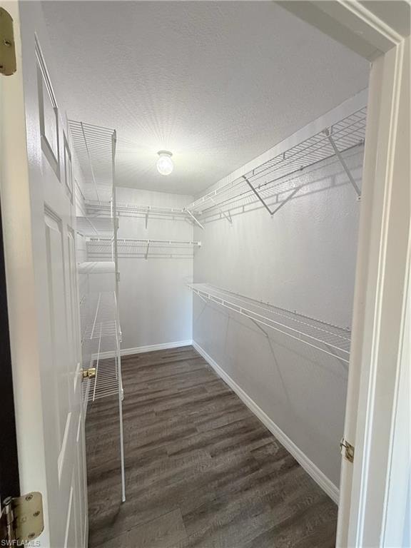 Walk-in closet featuring wood-finish flooring, white wire shelving, a ceiling light fixture, and white baseboards