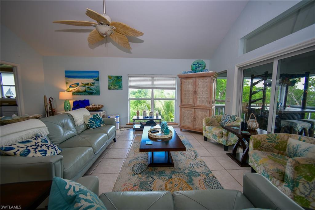 Bright living area featuring vaulted ceilings, tile flooring, a tropical-style ceiling fan, large windows, and sliding glass doors opening to an outdoor area