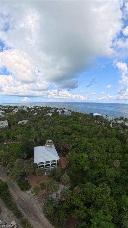 Coastal property featuring a metal roof, multiple balconies, a surrounding dense tree canopy, and direct proximity to the ocean