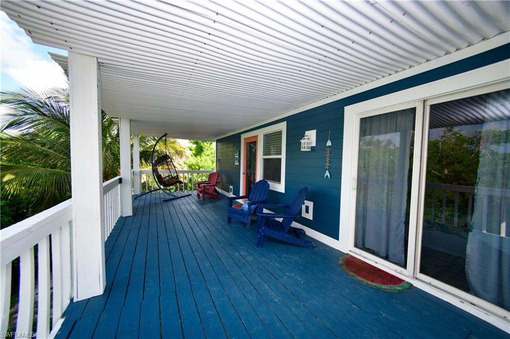 Expansive covered porch featuring a vibrant blue wood-finish deck, white railing, and a corrugated metal ceiling
