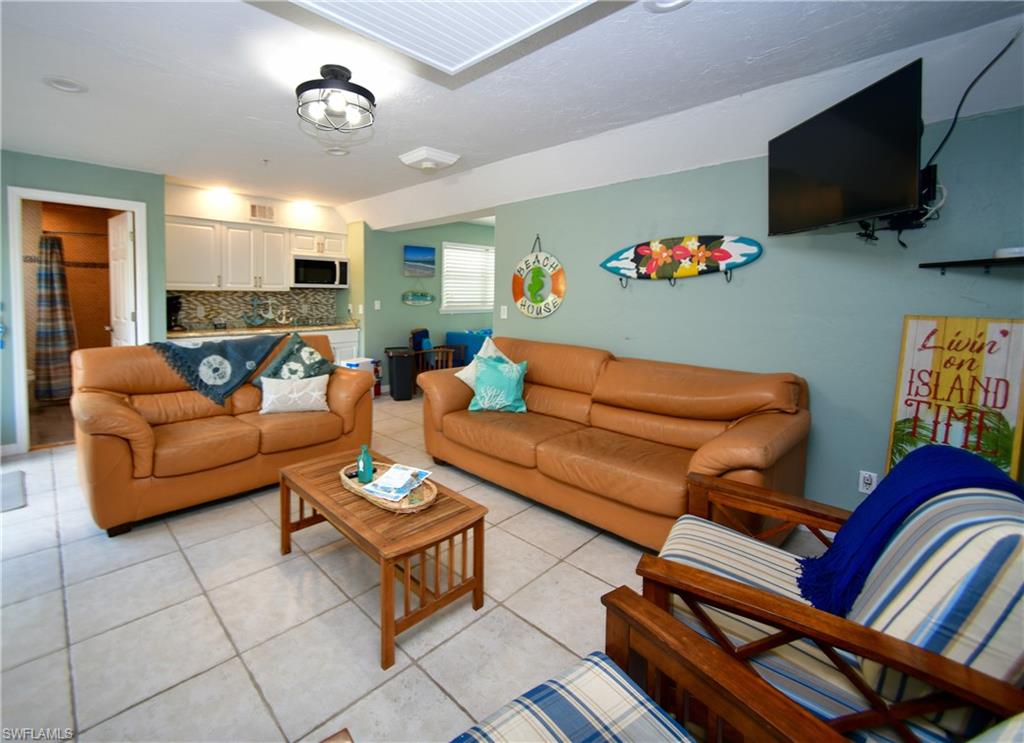 Open-concept living area with tiled flooring, a built-in kitchen area with white cabinetry, a patterned backsplash, and an integrated microwave