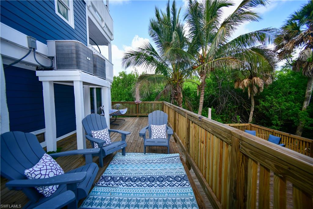 Expansive wood deck with a natural wood railing, featuring a vibrant blue and white patterned outdoor rug and a backdrop of established palm trees