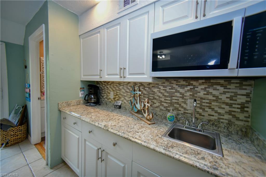 Kitchenette featuring white cabinetry, granite-patterned countertops, a stainless steel sink, and a multi-tone mosaic tile backsplash