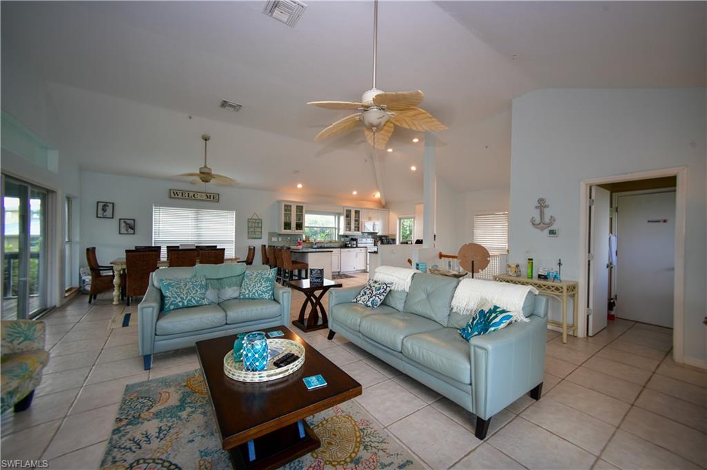 Spacious open-concept living area featuring vaulted ceilings, tile flooring, and multiple ceiling fans