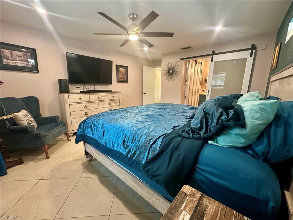 Bedroom featuring tile flooring, a ceiling fan with integrated lighting, and a sliding barn door with frosted glass panel