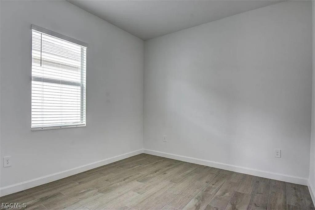 Bright interior room featuring a window with white blinds, wood-finish flooring, white baseboards, and neutral wall paint