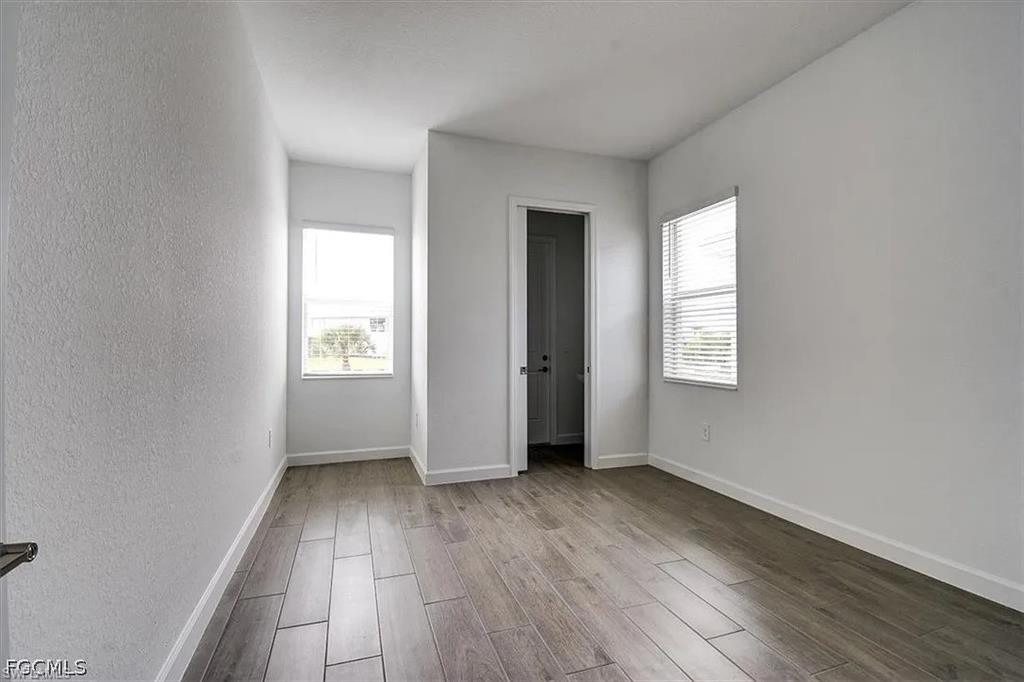 Spacious room featuring wood-finish flooring, two windows with blinds, and a white interior door