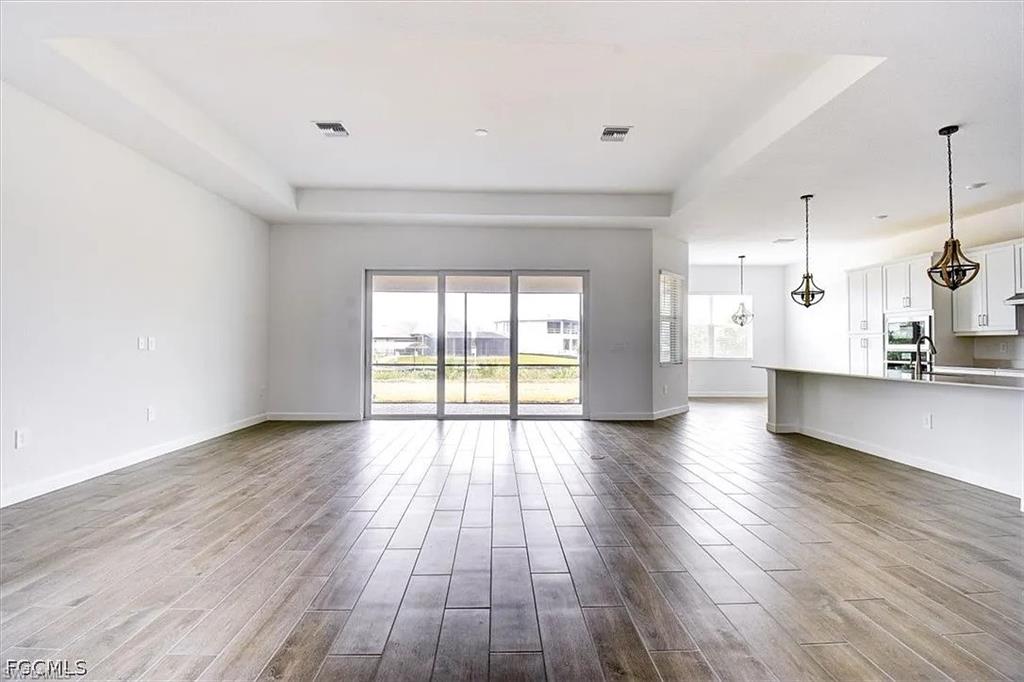 Expansive open-concept room featuring wood-finish tile flooring, tray ceiling, and sliding glass doors to the exterior