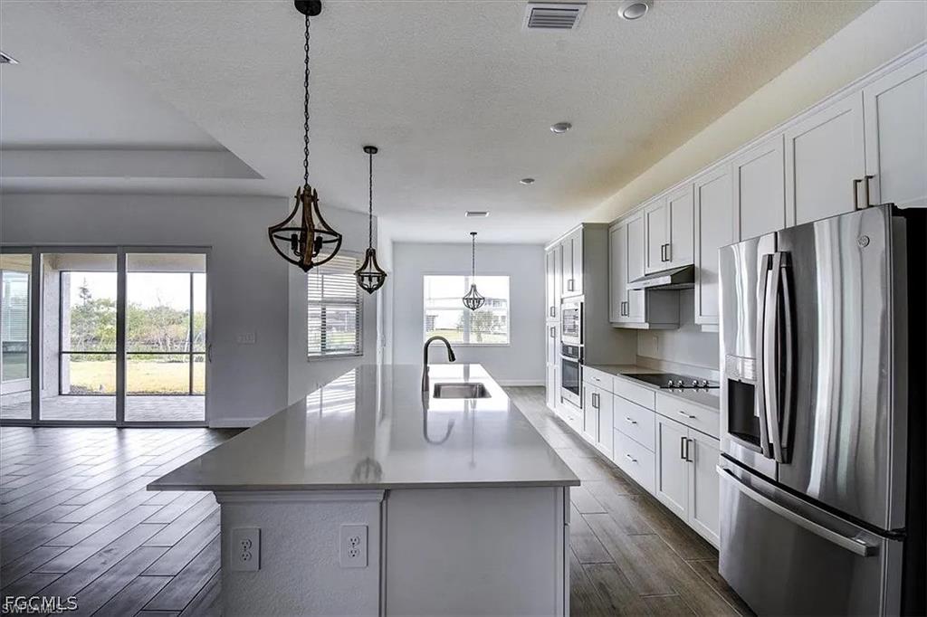 Spacious kitchen featuring a large central island with an undermount sink, white shaker cabinetry with dark hardware, stainless steel appliances, and wood-finish flooring